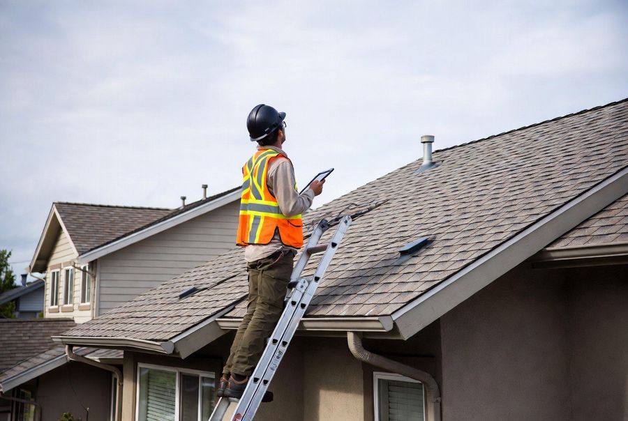 Roofer on a ladder inspecting a roof with a tablet